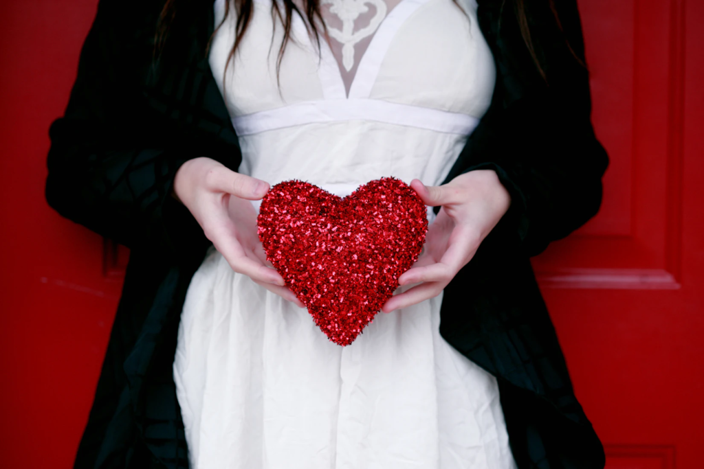 Alt tag: A woman in a white dress holds a red heart in front of her stomach. 