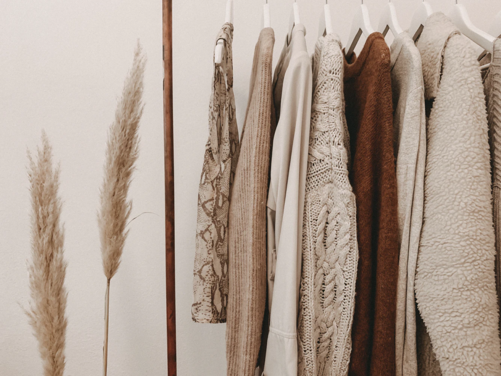A rack of beige-colored clothing next to a tall, brown plant.