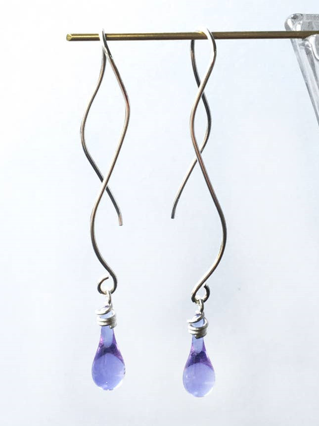 A pair of twisted metal earrings with purple tear-drop pendants from a minimalist capsule wardrobe. 