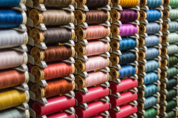 Multiple bobbins of colored thread used in cheap sustainable clothing stacked in rows.